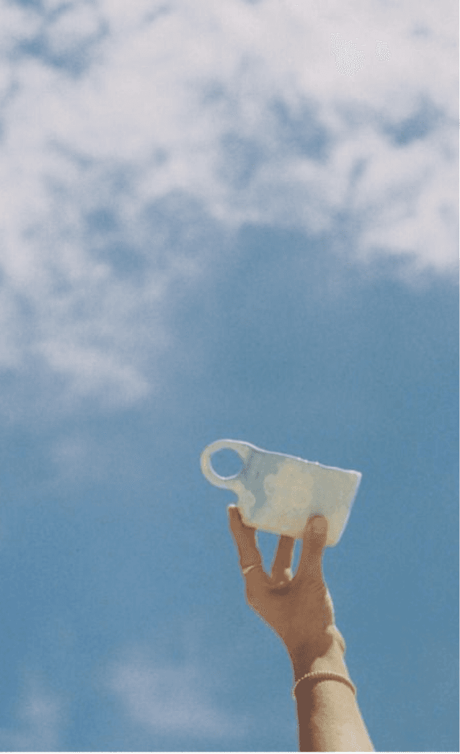 Mão erguendo uma xícara de cerâmica contra o céu azul